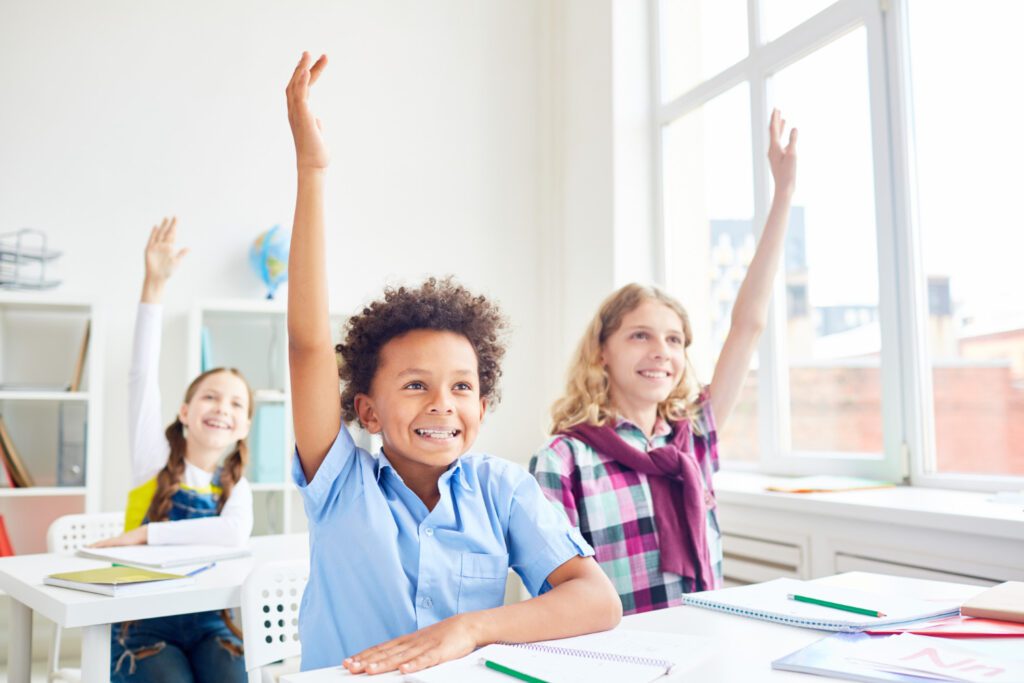 students in classroom raising their hands